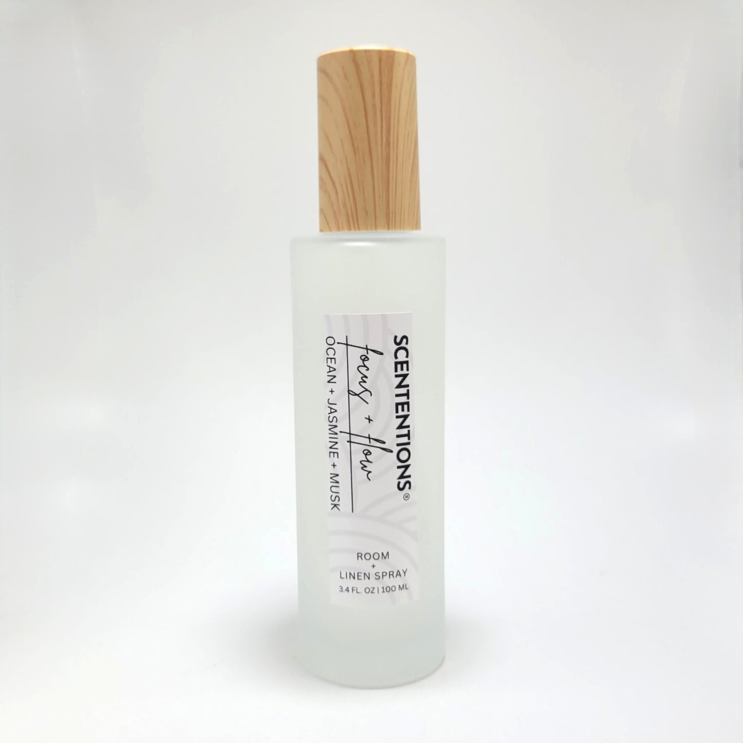 Focus + Flow room and linen spray in frosted glass bottle with wood cap on white background.
