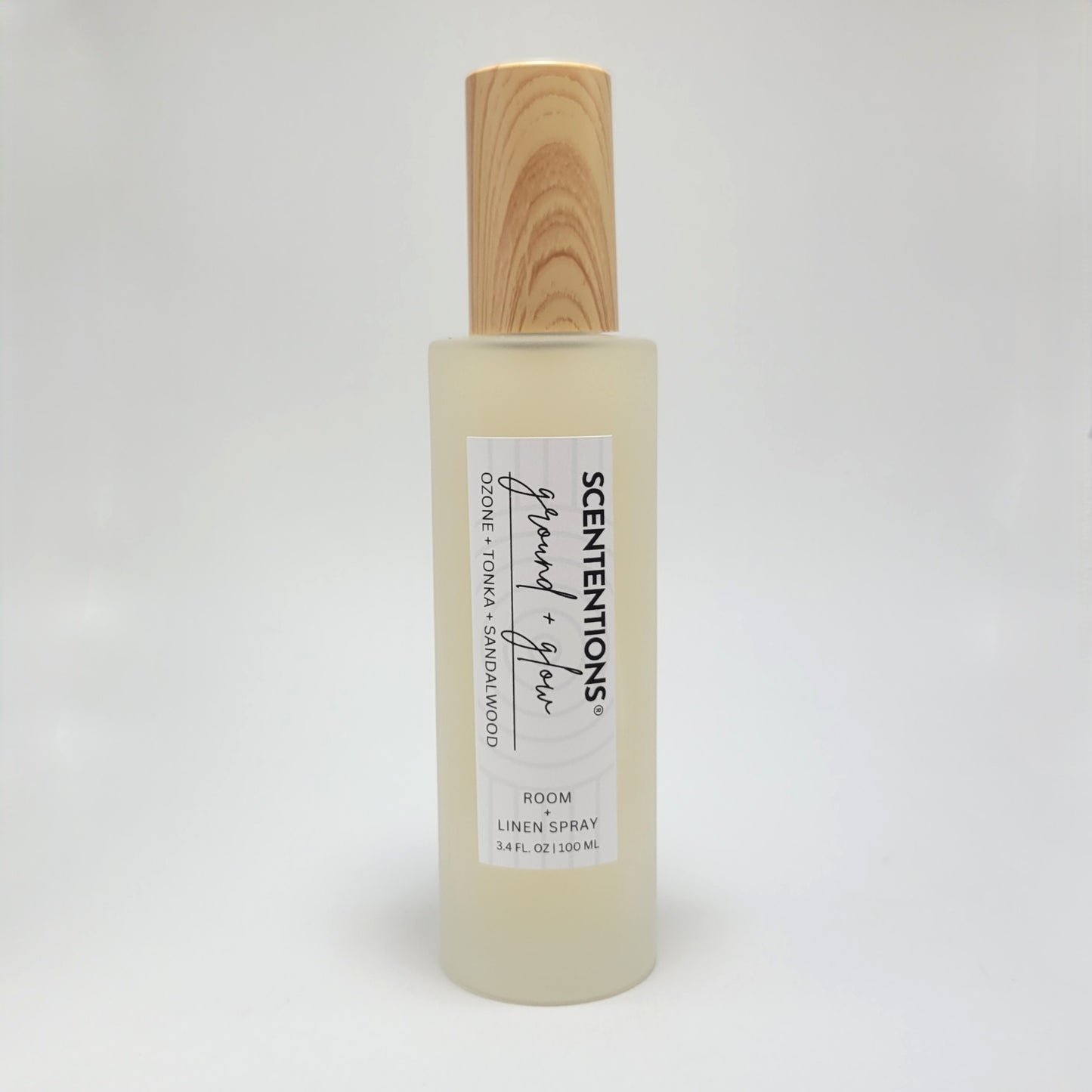 Ground + Glow room and linen spray in frosted glass bottle with wood cap on white background.