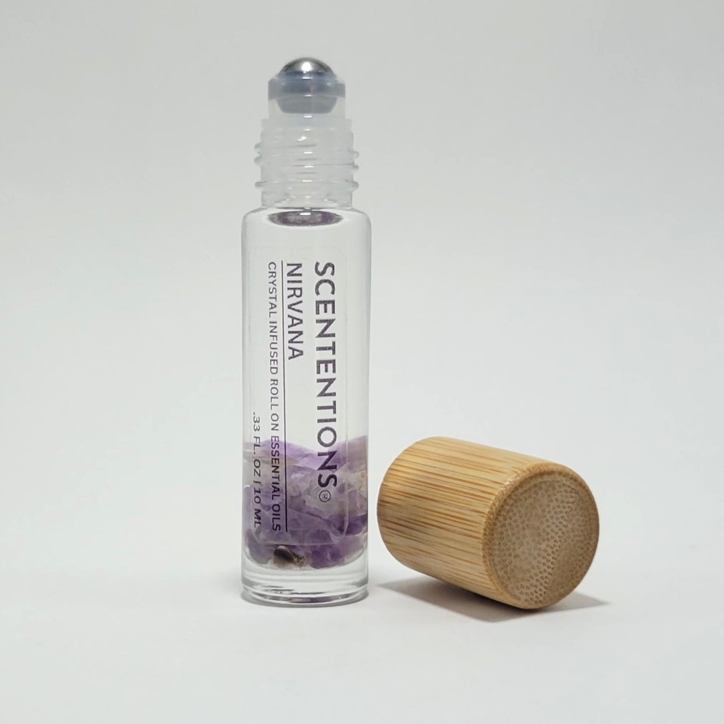 Open crystal infused roll-on bottle with visible Amethyst crystals and bamboo cap beside it