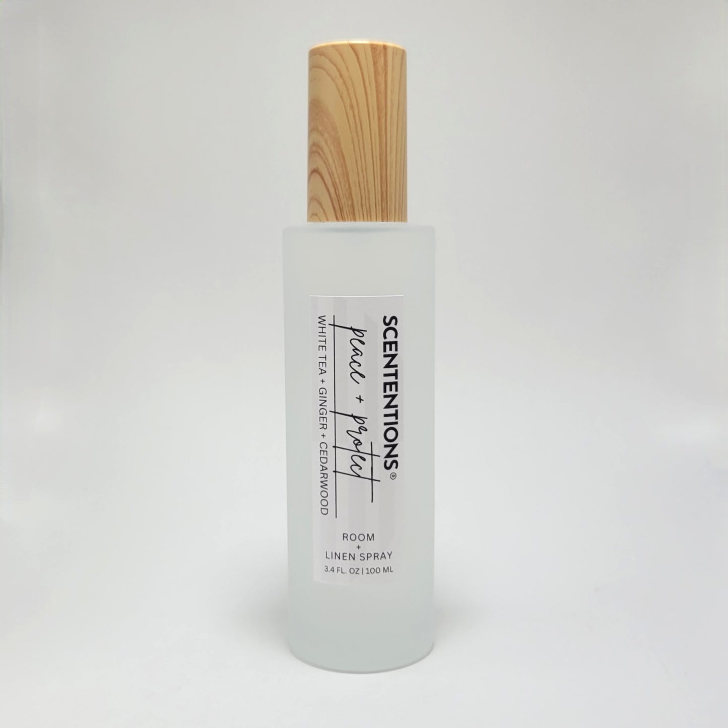 Peace + Protect room and linen spray in frosted glass bottle with wood cap on white background.