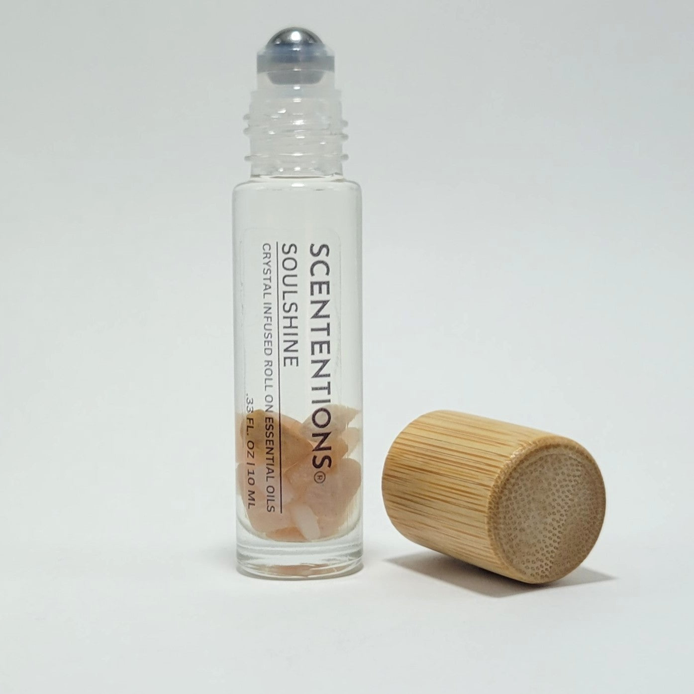 Open crystal infused roll-on bottle with visible Sunstone crystals and bamboo cap beside it.