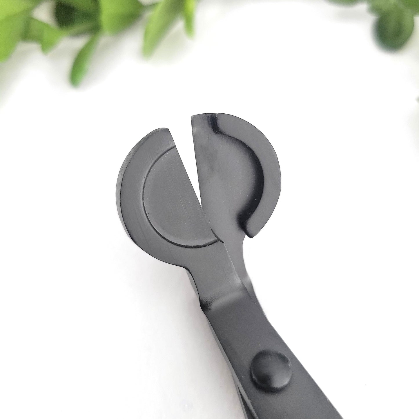 Close-up of matte black metal wick cutter showing angled design for trimming candle wicks cleanly and safely.
