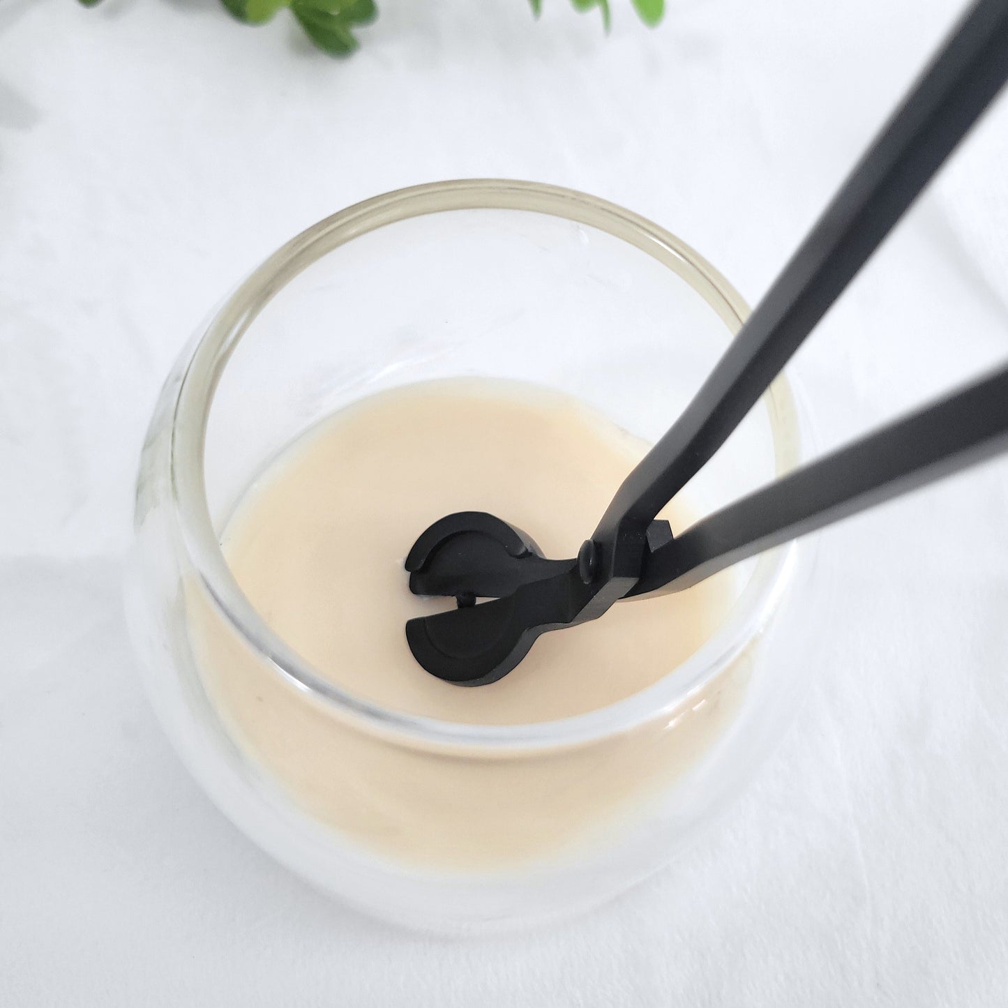 Matte black wick cutter trimming the wick of a Scententions candle to maintain an even burn and longer-lasting fragrance.