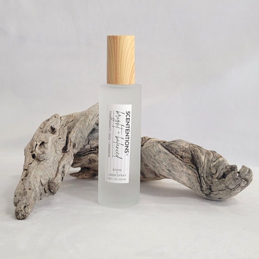 Frosted glass room and linen spray bottle labeled Bright + Balanced on a natural wood background.