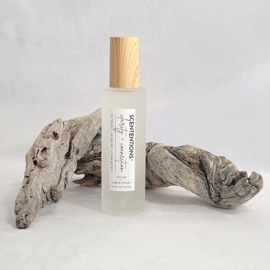 Frosted glass room and linen spray bottle labeled Clarity + Connection on a natural wood background.