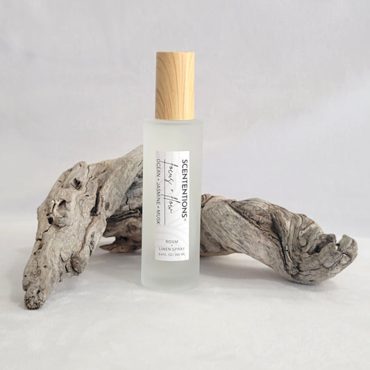 Frosted glass room and linen spray bottle labeled Focus + Flow on a natural wood background.