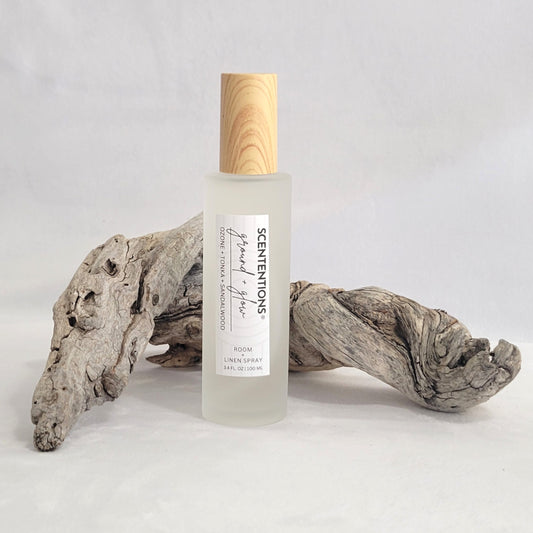 Frosted glass room and linen spray bottle labeled Ground + Glow on a natural wood background.