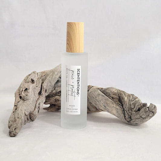 Frosted glass room and linen spray bottle labeled Peace + Protect on a natural wood background.