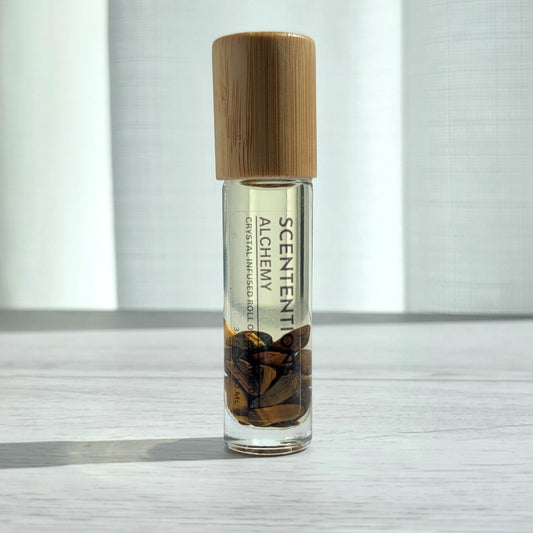 Crystal infused roll-on essential oil with Tiger’s Eye crystals and bamboo lid on white wood surface in natural light