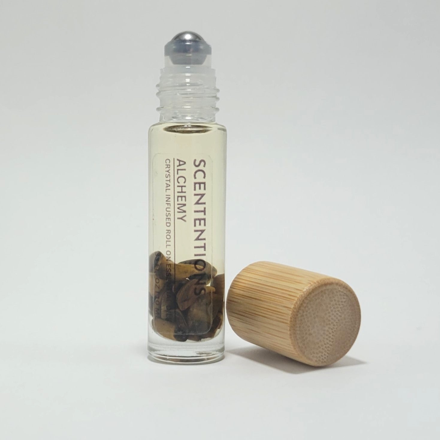 Open crystal infused roll-on bottle with visible Tiger’s Eye crystals and bamboo cap beside it