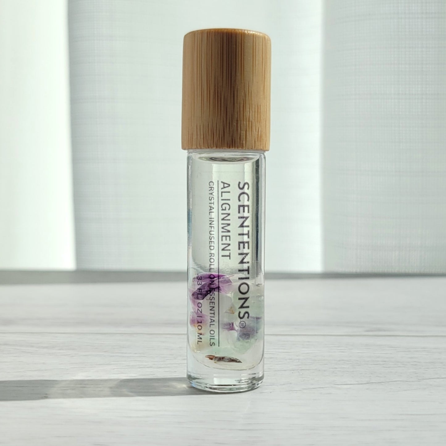 Crystal infused roll-on essential oil with Fluorite crystals and bamboo lid on white wood surface in natural light