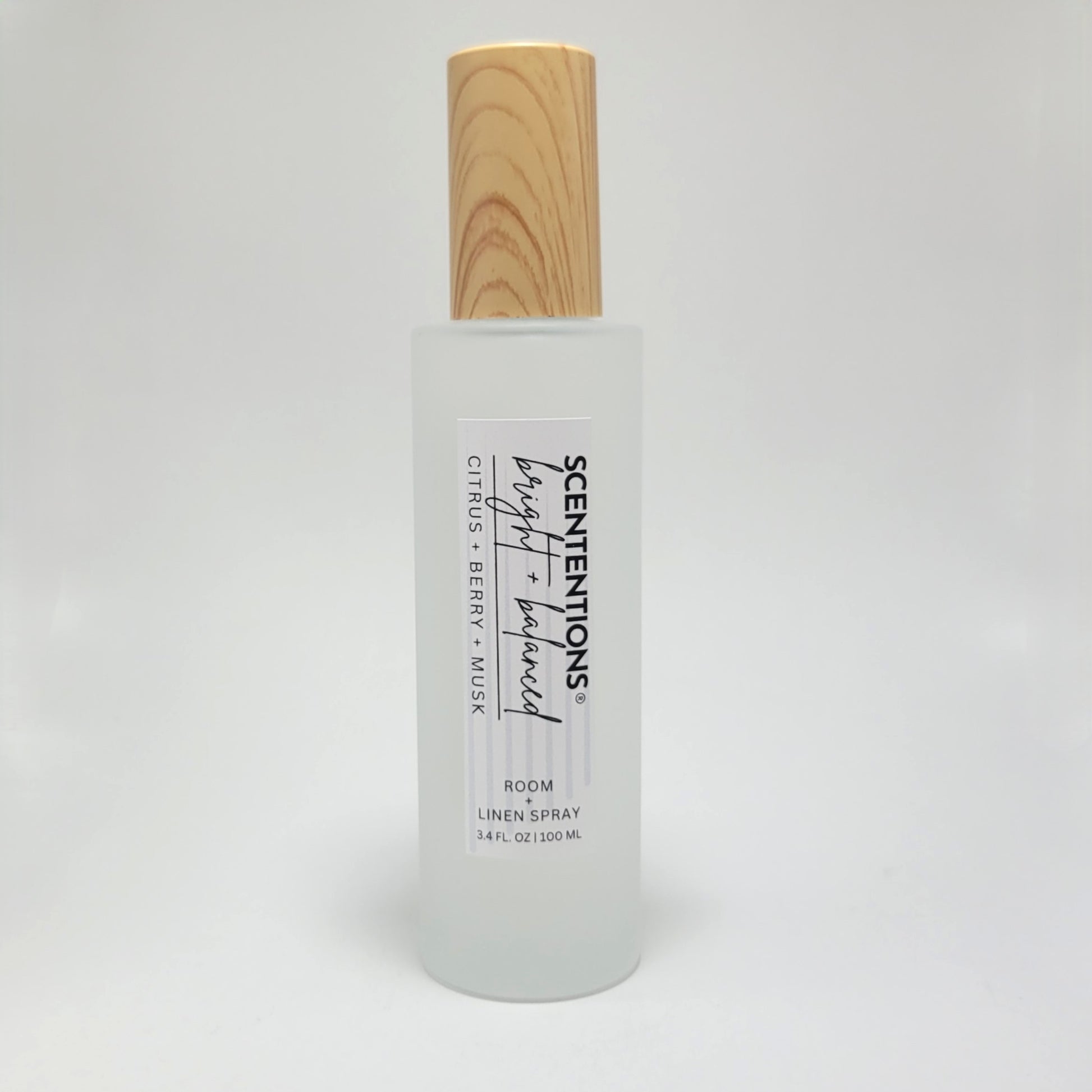 Bright + Balanced room and linen spray in frosted glass bottle with wood cap on white background.