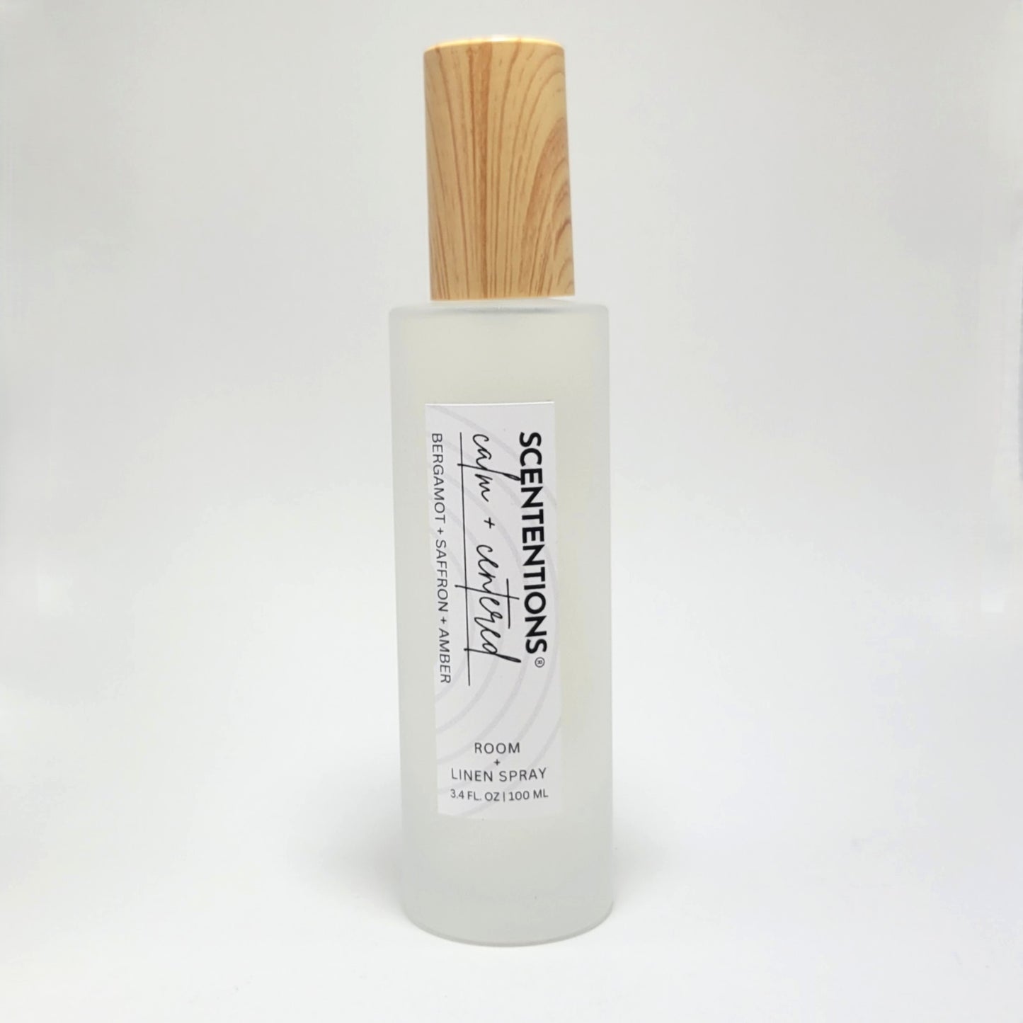 Calm + Centered room and linen spray in frosted glass bottle with wood cap on white background.