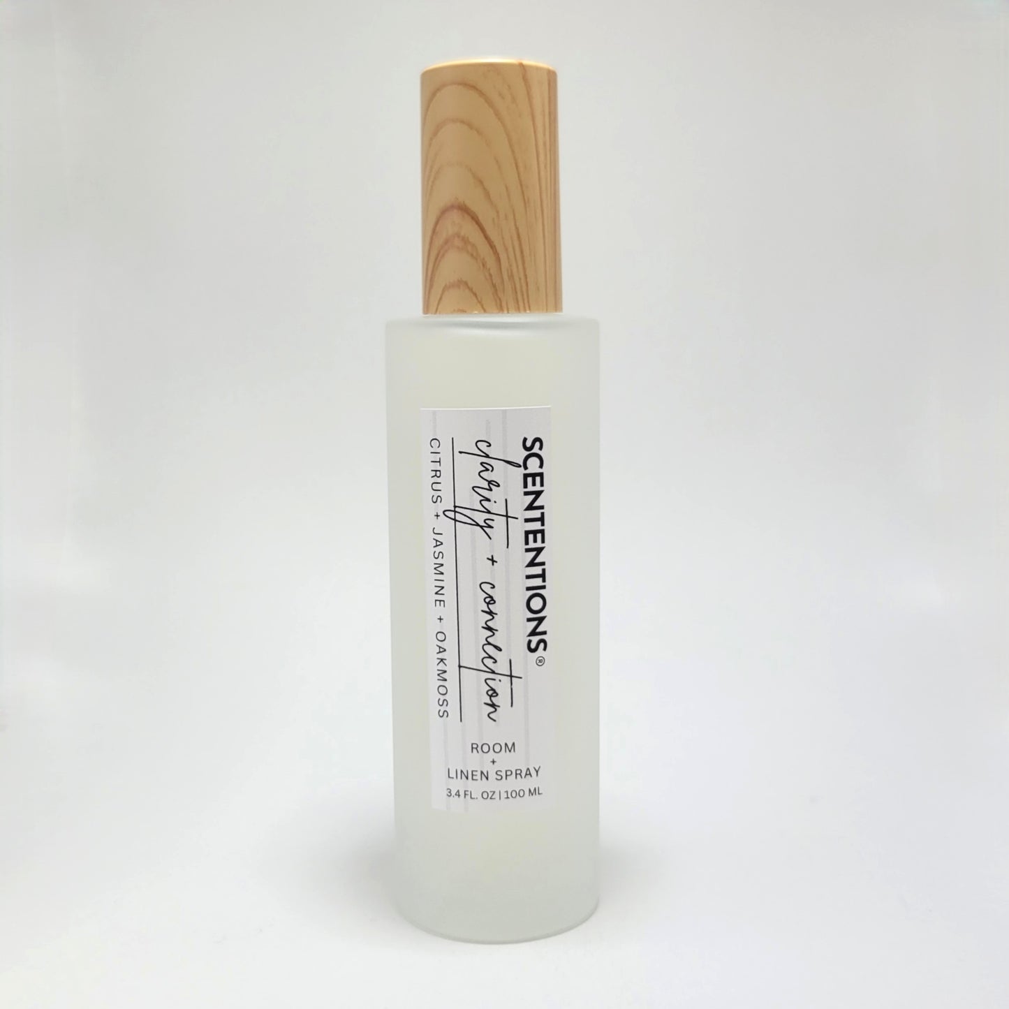 Clarity + Connection room and linen spray in frosted glass bottle with wood cap on white background.