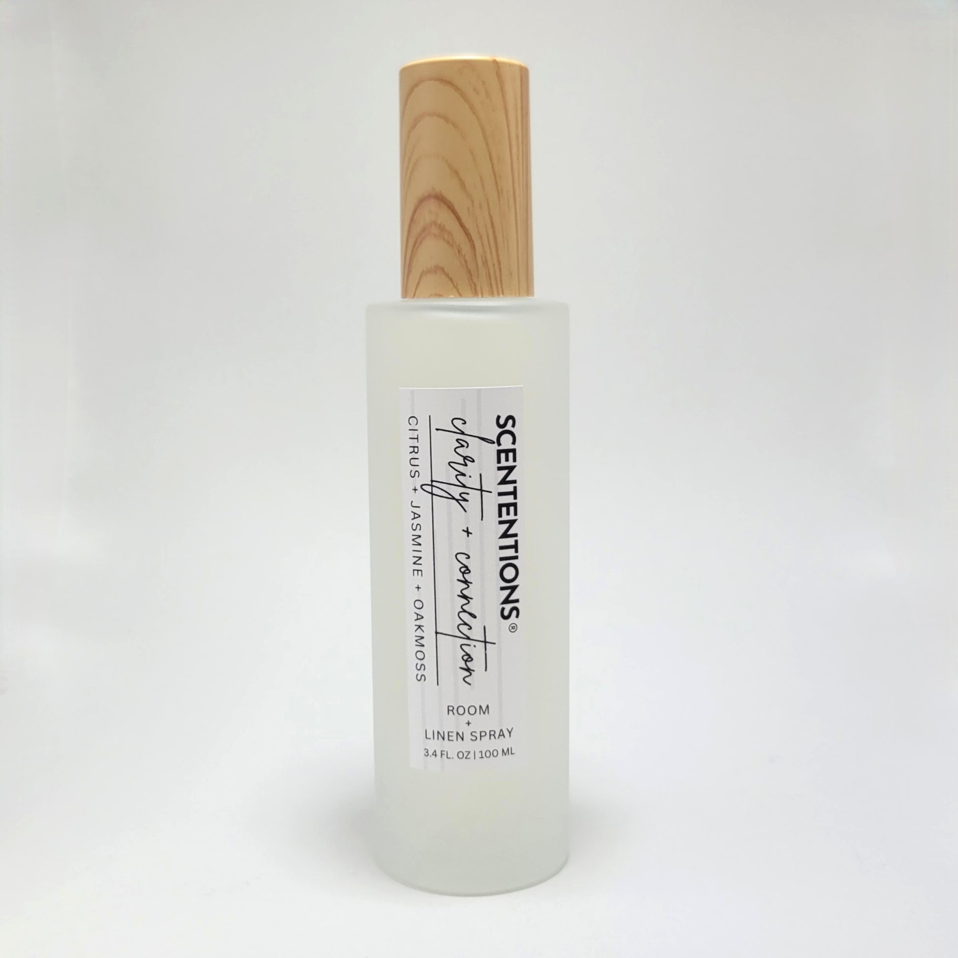 Clarity + Connection room and linen spray in frosted glass bottle with wood cap on white background.
