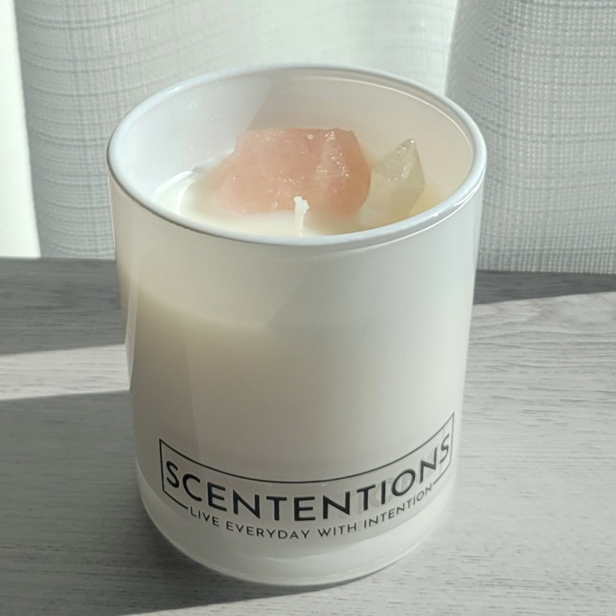 Coasts + Coconuts Wanderlust crystal coconut wax candle in clear glass vessel with rose quartz and clear quartz crystals in natural sunlight.