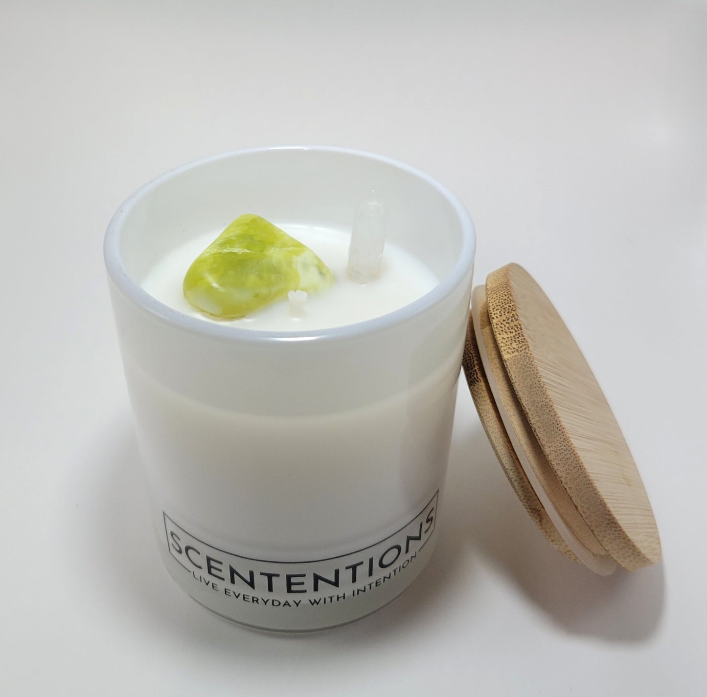 Dream + Discover Wanderlust crystal coconut wax candle with noble serpentine and clear quartz double-sided point and bamboo lid beside jar. 