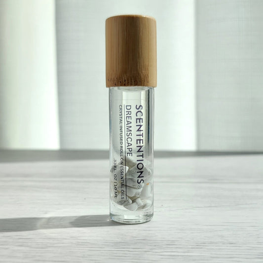 Crystal infused roll-on essential oil with Howlite crystals and bamboo lid on white wood surface in natural light