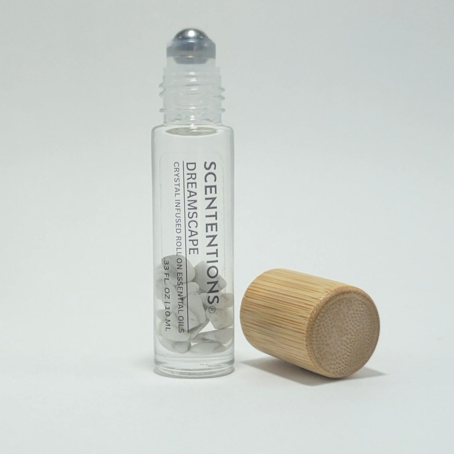 Open crystal infused roll-on bottle with visible Howlite crystals and bamboo cap beside it