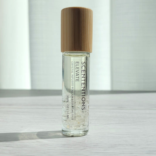 Crystal infused roll-on essential oil with Clear Quartz crystals and bamboo lid on white wood surface in natural light