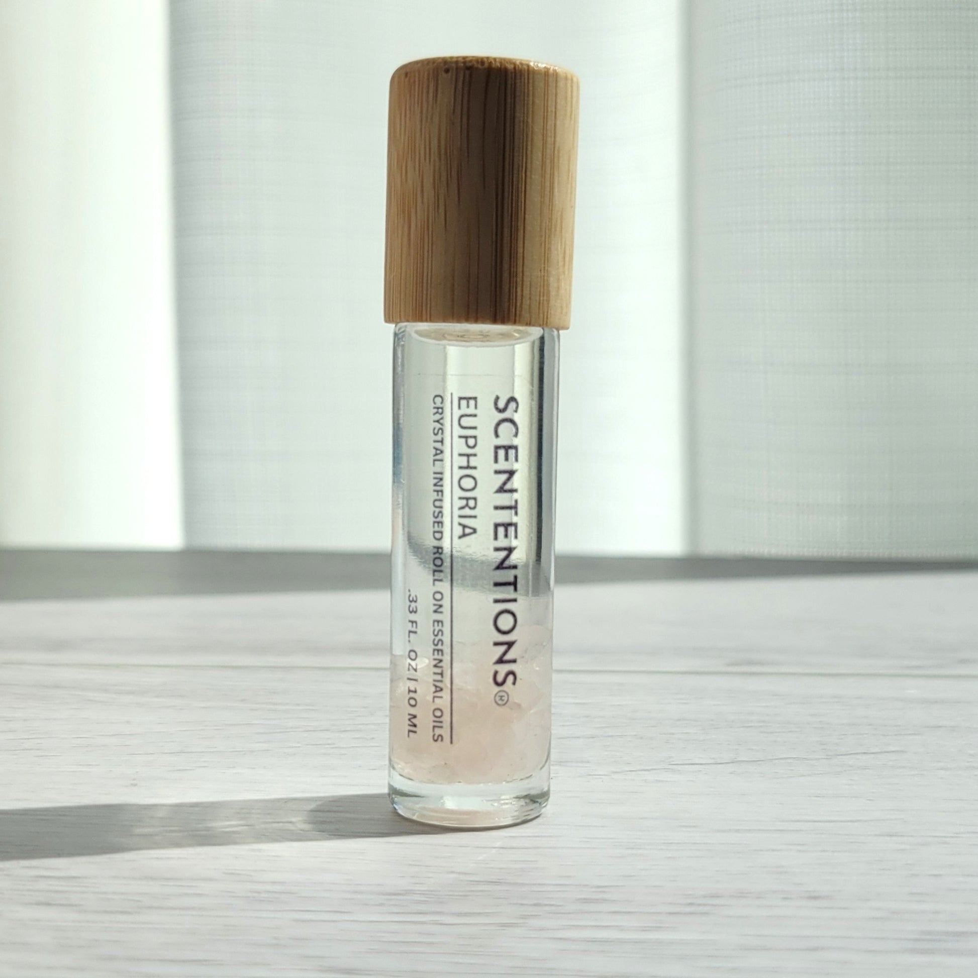 Crystal infused roll-on essential oil with Rose Quartz crystals and bamboo lid on white wood surface in natural light