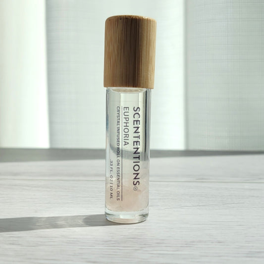 Crystal infused roll-on essential oil with Rose Quartz crystals and bamboo lid on white wood surface in natural light