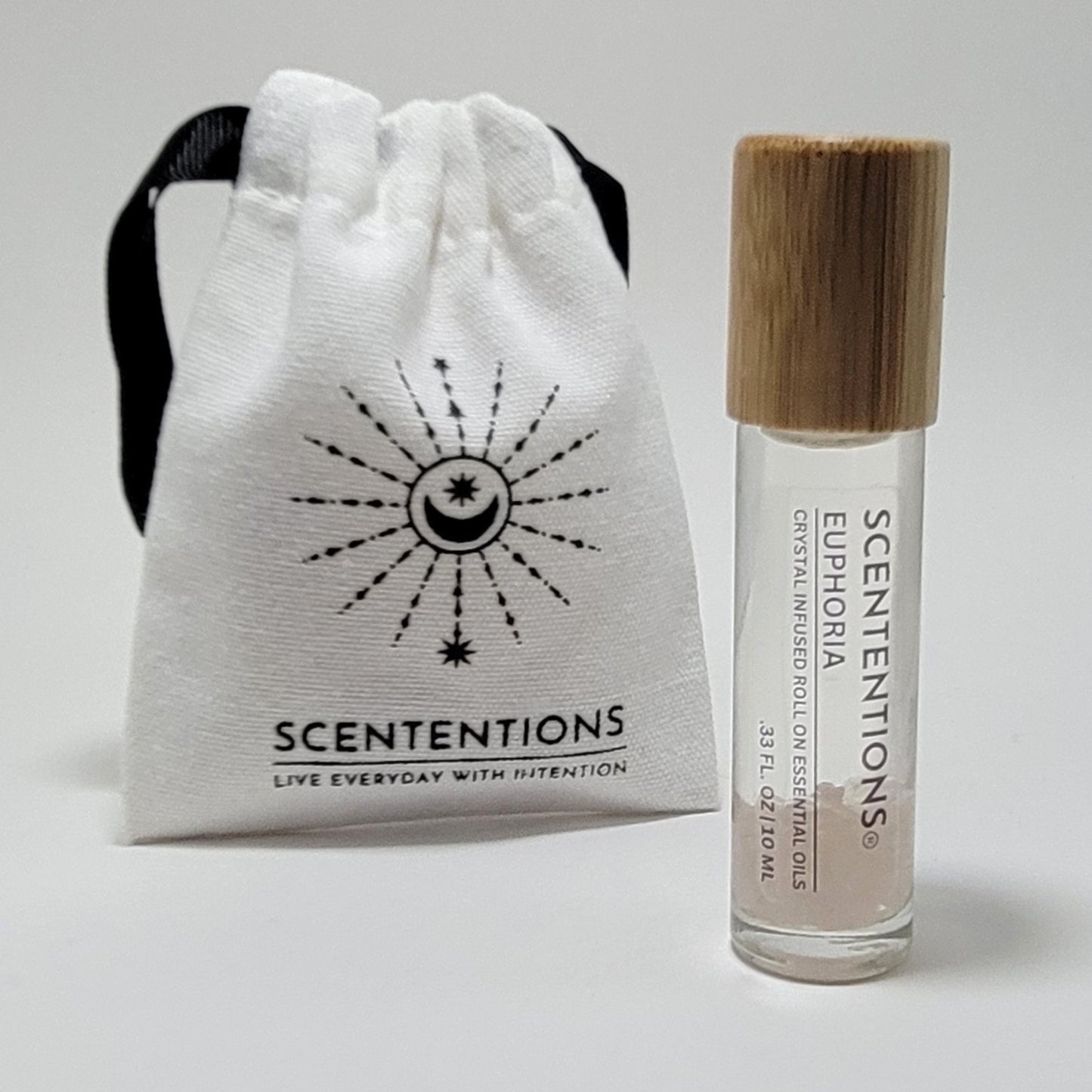 Crystal infused roll-on essential oil with Rose Quartz crystals next to Scententions canvas pouch