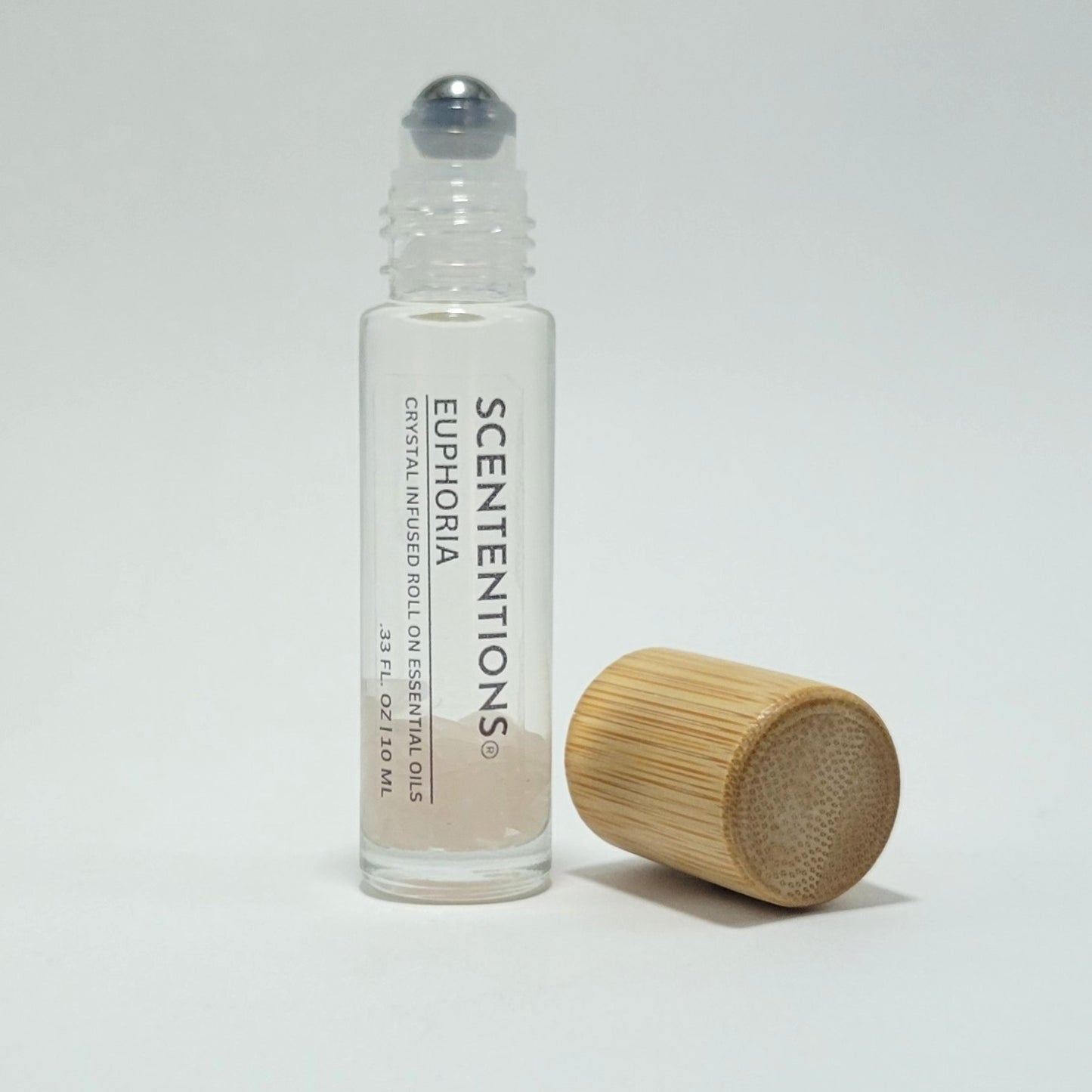 Open crystal infused roll-on bottle with visible Rose Quartz crystals and bamboo cap beside it