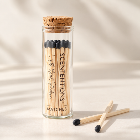 SCENTENTIONS long black-tip matches in a clear glass jar with cork lid, styled with loose matches on a soft cream background.