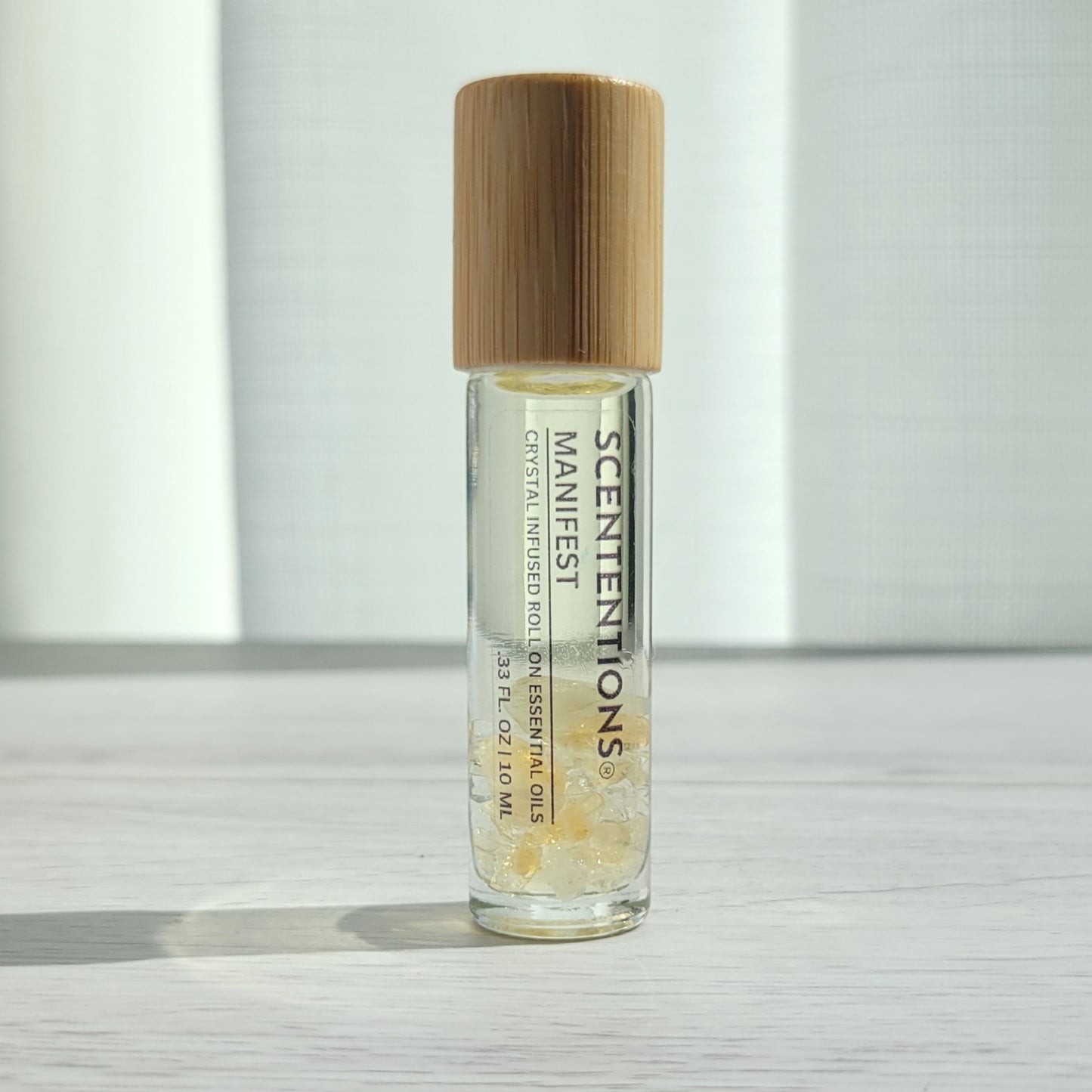 Crystal infused roll-on essential oil with Citrine crystals and bamboo lid on white wood surface in natural light