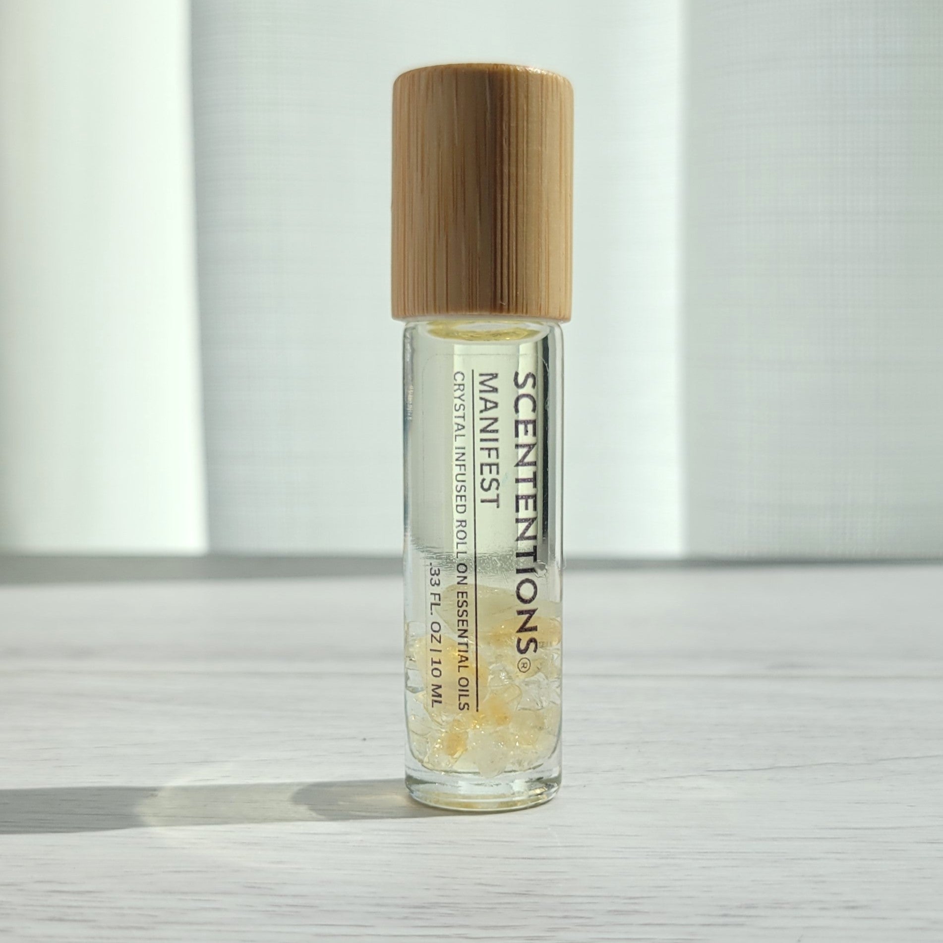 Crystal infused roll-on essential oil with Citrine crystals and bamboo lid on white wood surface in natural light