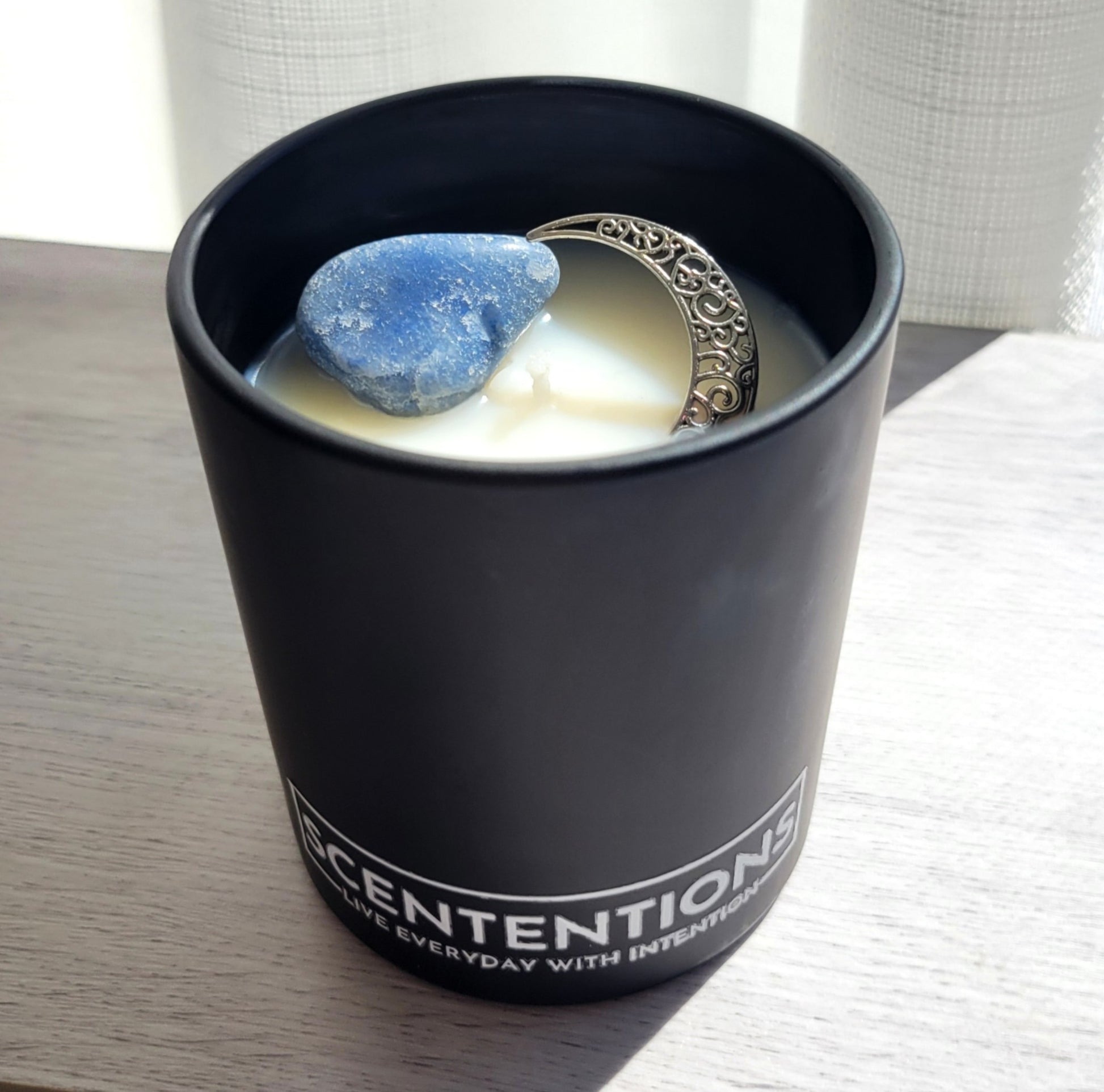 Moon + Tide Moon Collection crystal coconut wax candle in clear glass vessel with clear quartz and silver moon charm in natural sunlight.