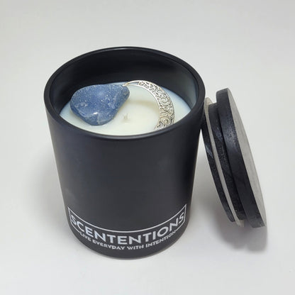 Moon + Tide Moon Collection crystal coconut wax candle with clear quartz, silver moon charm, and black wood lid beside jar.