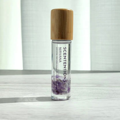 Crystal infused roll-on essential oil with Amethyst crystals and bamboo lid on white wood surface in natural light