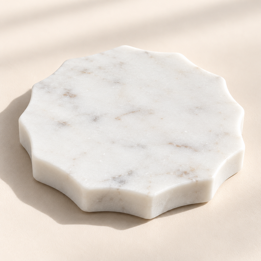 Scalloped white marble candle coaster with subtle natural veining and softly curved edges, photographed on a light cream background.