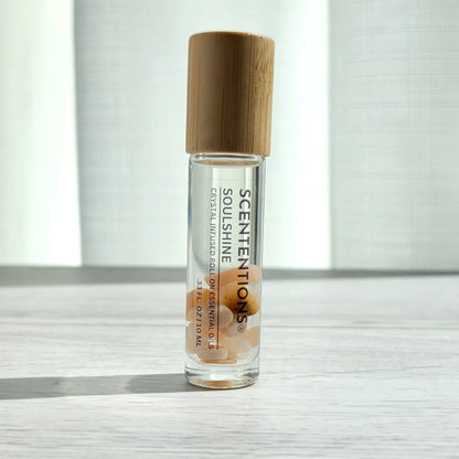 Crystal infused roll-on essential oil with Sunstone crystals and bamboo lid on white wood surface in natural light.